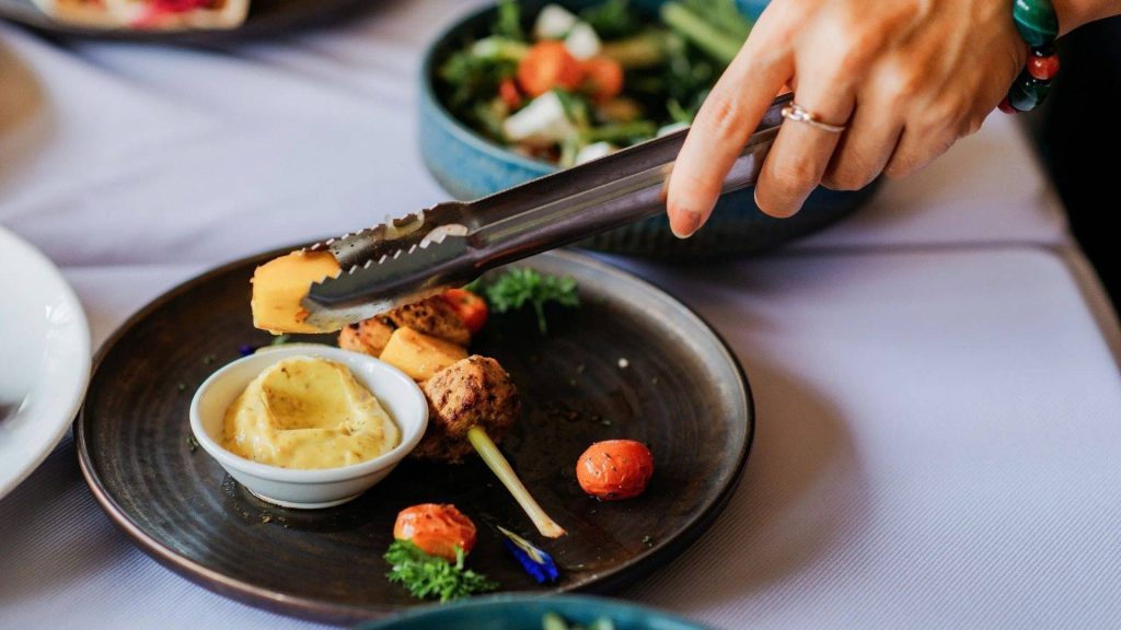 hand serving food onto a plate with dips, veggies, and small skewers