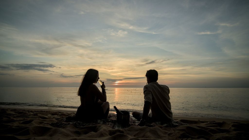 two people sitting together on a quiet beach, watching the sunset